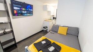 Ein kleines Hotelzimmer mit Bett, Wandfernseher, einer kleinen Küchenzeile und einer Schrankwand.