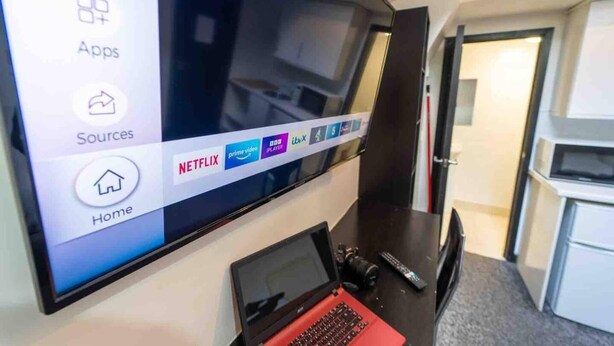 Ein Hotelzimmer mit einem großen Flachbildfernseher an der Wand, der eine Fernseh-Oberfläche mit App-Symbolen zeigt.