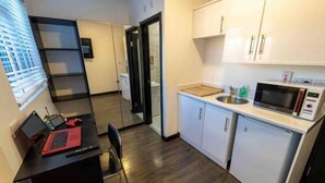 A compact kitchen with white cabinets, a microwave, and a sink. There's a small dining area with a black table and a red laptop. - Cosy top Floor Studio Available Near the City! (Birmingham)