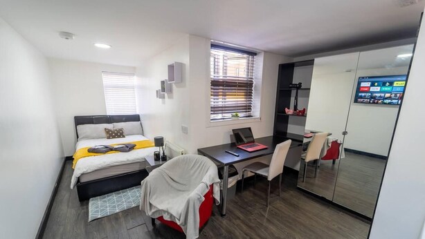 A compact hotel room with a bed, a desk with a laptop, a chair, and a small table. - Cosy top Floor Studio Available Near the City! (Birmingham)