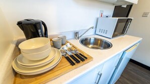 A kitchenette with a sink, microwave, kettle, and stacked dishes. - Cosy top Floor Studio Available Near the City! (Birmingham)