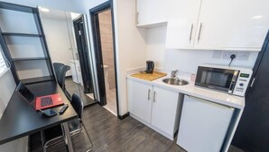 A compact kitchen with a microwave, toaster, and sink. There's a small dining area with a laptop and chair. - Large Studio Available on First Floor! (Birmingham)