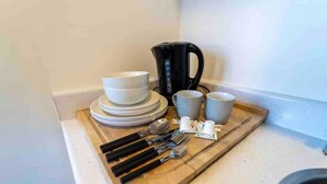 A kitchen counter with stacked white bowls, a black coffee maker, blue cups, and utensils on a wooden tray. - Modern Studio Available Close to the City (Birmingham)