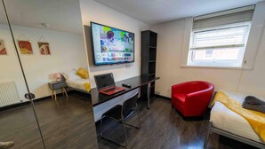 A modern room with a bed, a desk with a laptop, a red chair, and a TV displaying a streaming service interface. - Modern Studio Available Close to the City (Birmingham)