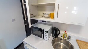 A compact kitchenette with a microwave, coffee maker, and a stainless steel sink. - Modern Studio Available Close to the City (Birmingham)