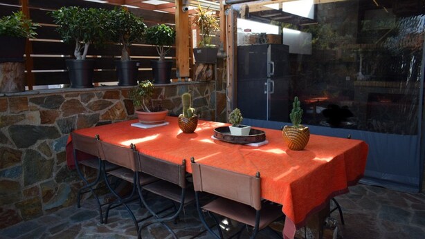 An outdoor patio with a stone wall, a wooden pergola, and a table covered with a red tablecloth. - MTC-Jasmine's House (Markopoulo Mesogaias)