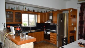 A modern kitchen with wooden cabinets, a stainless steel refrigerator, and a window providing natural light. - MTC-Jasmine's House (Markopoulo Mesogaias)