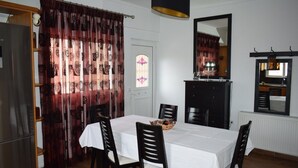 A dining area with a table set for four, a black cabinet, a mirror, and a window with curtains. - MTC-Jasmine's House (Markopoulo Mesogaias)