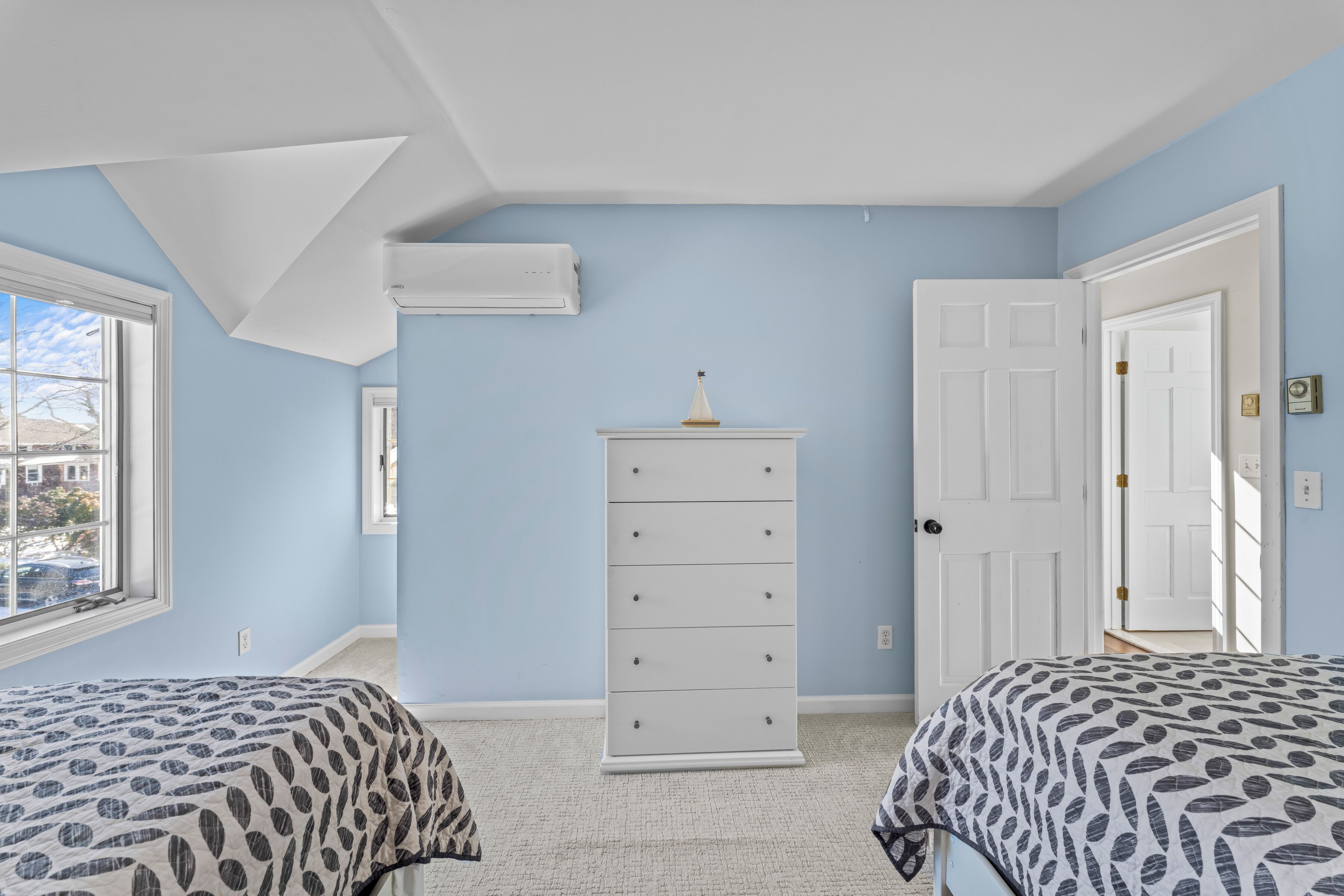 Une chambre avec deux lits, une commode blanche et une fenêtre.