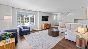 Una sala de estar moderna con un sofá, un sillón, una mesa de centro y un televisor montado en la pared.