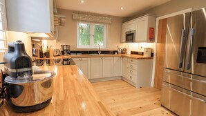 A modern kitchen with wooden countertops, stainless steel appliances, and a window with a view of greenery. - Beech Lea (Ulverston)