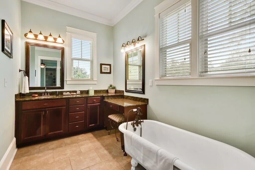 A bathroom with a freestanding bathtub, vanity with a mirror, and two windows with blinds.