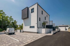 A modern building with a parking lot, a van, and a staircase leading to a second-floor entrance. - Holiday apartment with pool (Njivice)
