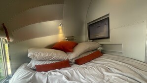 Une chambre à coucher avec un lit, des oreillers, une télévision et une fenêtre.