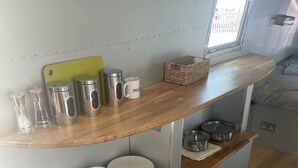 Un coin cuisine avec des étagères en bois où sont rangés les ustensiles de cuisine, une planche à découper et une fenêtre donnant sur un paysage agréable.