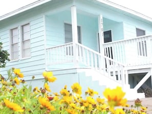 Welcome to 1701, a charming home with a white porch and a staircase leading to the entrance, surrounded by vibrant flowers and lush foliage.