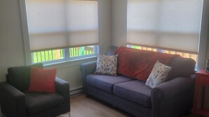 A living room with two sofas, a patterned rug, and a window with blinds. - Cozy North Shore two bedroom cottage (York)