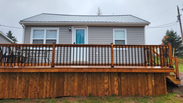 A single-story house with a grey exterior and a blue door, a wooden deck with a railing, and a visible power line in the background. - Cozy North Shore two bedroom cottage (York)