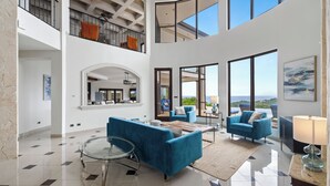 A spacious, modern living area with a high ceiling, large windows, and a balcony overlooking the sea. - Luxury House in Mar Vista, Flamingo, Cabo Velas (Playa Flamingo)