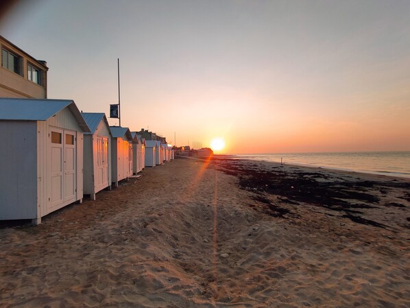Uma fileira de cabanas de praia com o pôr do sol ao fundo.