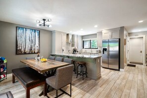 A modern kitchen with a central island, stainless steel appliances, and a dining area with a wooden table and chairs.