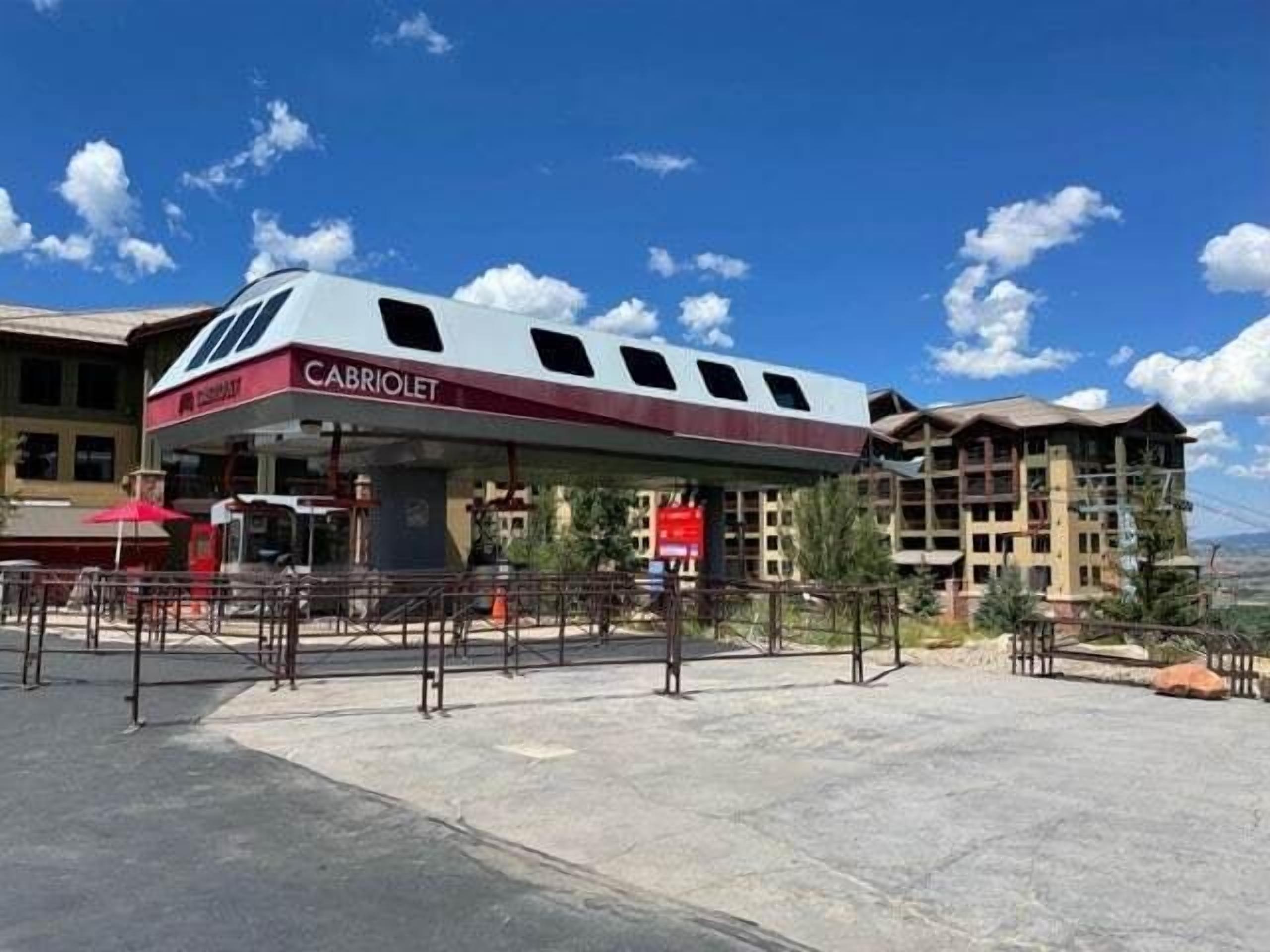 A gas station named 'CABRIOLET' with a modern design, outdoor seating, and a view of the surrounding buildings and landscape.