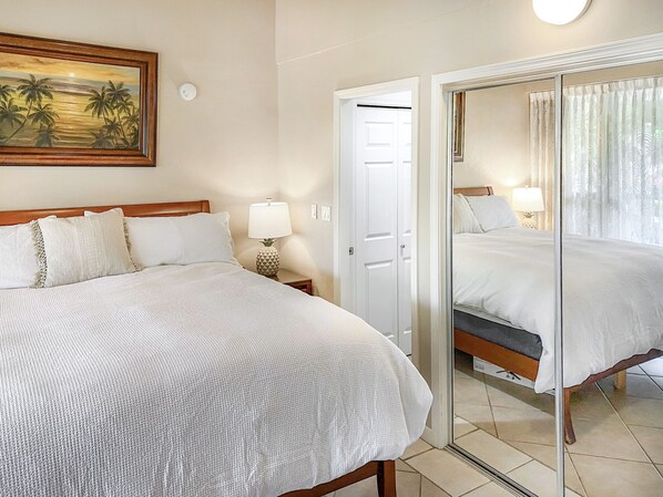 A hotel room with a bed, a nightstand with a lamp, a painting on the wall, and a door leading to another room.