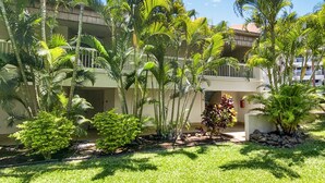 A hotel with multiple floors, surrounded by lush greenery and palm trees. - Renovated 1BR at Maui Banyan - Pool, Hot Tub, A/C (Kihei)