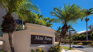 A sign for 'Mani Banyan' with a street view in the background. - Renovated 1BR at Maui Banyan - Pool, Hot Tub, A/C (Kihei)