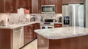 A modern kitchen with brown cabinets, stainless steel appliances, granite countertops, and a built-in microwave. - Renovated 1BR at Maui Banyan - Pool, Hot Tub, A/C (Kihei)