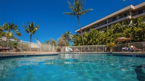 A pool area with clear blue water, surrounded by palm trees and a building with balconies. - Renovated 1BR at Maui Banyan - Pool, Hot Tub, A/C (Kihei)