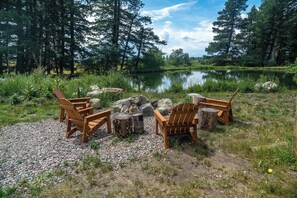 Järvenrantapaikka, jossa on puisia Adirondack-tyylisiä tuoleja aseteltu ympyrän muotoon nuotiopaikan ympärille. Nuotiopaikan ympärillä on kiviä ja puita.