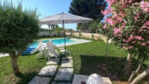 A pool area with a lounge chair and umbrella, surrounded by well-maintained grass and flowering bushes. - Villa Stella Marina (Punta Milocca)