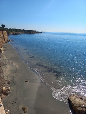 A beach with clear water, a rocky shoreline, and a distant view of the sea.