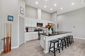 Een moderne keuken met witte kasten, een zwart aanrechtblad met barstoelen, een magnetron en een spoelbak.