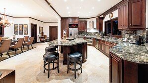 A spacious kitchen with dark wood cabinets, a granite countertop, and a central island with stools. - Playa Hermosa Luxe Villa • 4BR • 5BA • Infinity Pool & Ocean Views (Playa Hermosa)