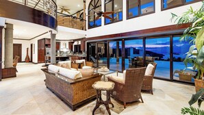 A spacious, elegantly designed interior with a high ceiling, large windows offering a view of the outdoors, and a cozy seating area with wicker furniture. - Playa Hermosa Luxe Villa • 4BR • 5BA • Infinity Pool & Ocean Views (Playa Hermosa)