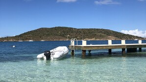 A clear waterfront with a dock extending into the water, a small boat moored at the dock, and a hilly landscape in the background. - Old World Caribbean with new world amenities (Belle Vue)