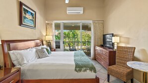 A hotel room with a bed, a TV, a chair, a table, and a balcony with a view of greenery. - ON SALE! Cozy Maui Studio With Beach + Pool (Kihei)