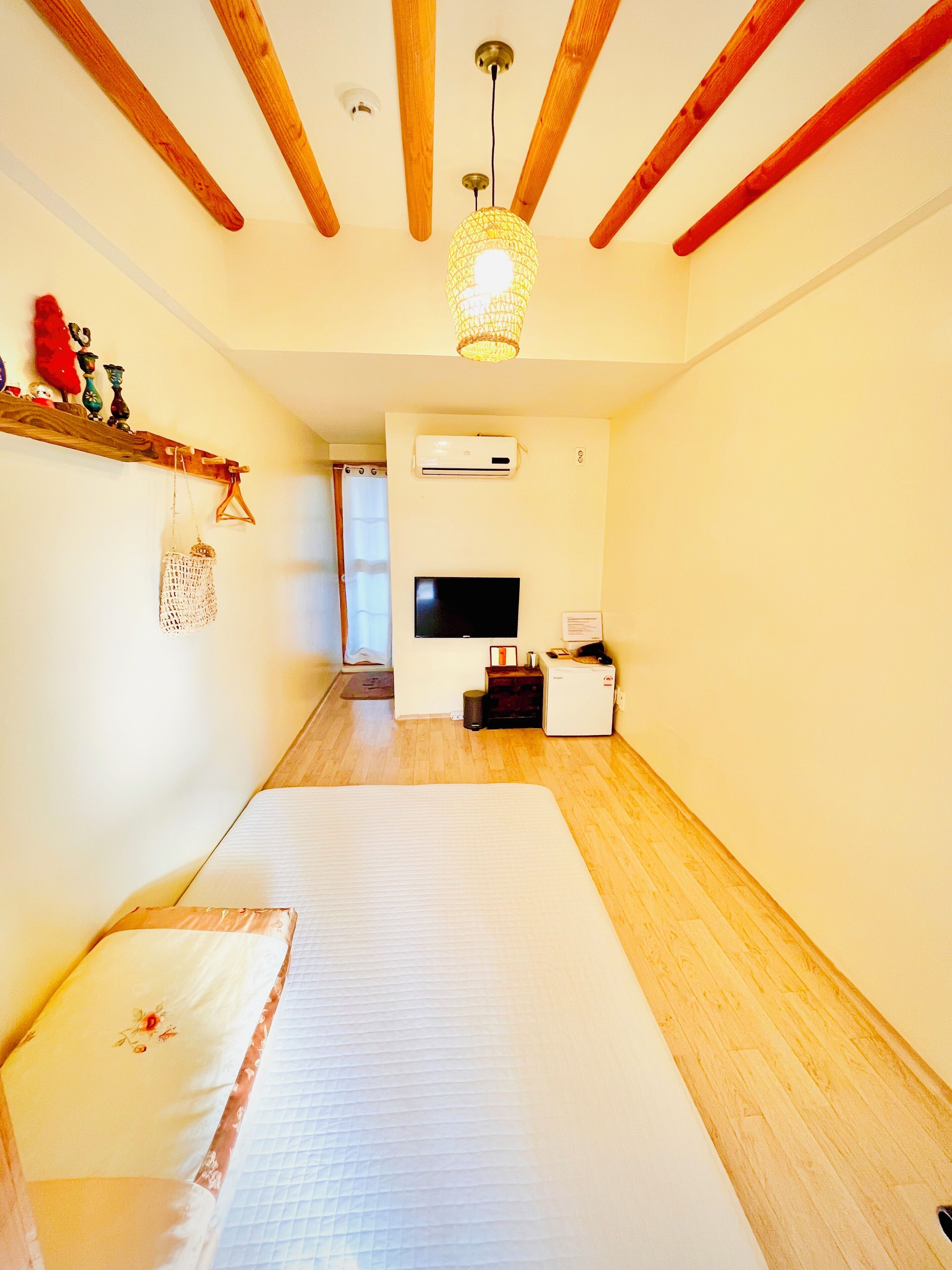 A room with a bed, a TV, an air conditioner, and a wooden ceiling.