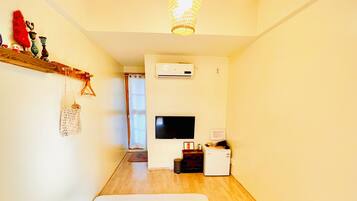 A room with a bed, a TV, an air conditioner, and a wooden ceiling.