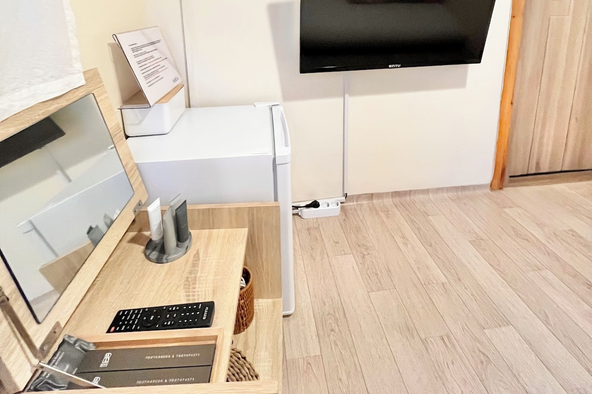 Ein Zimmer mit einem an der Wand montierten Flachbildfernseher, einem Schreibtisch inklusive Tastatur, einem kleinen Tisch mit Korb und einer Klimaanlage.