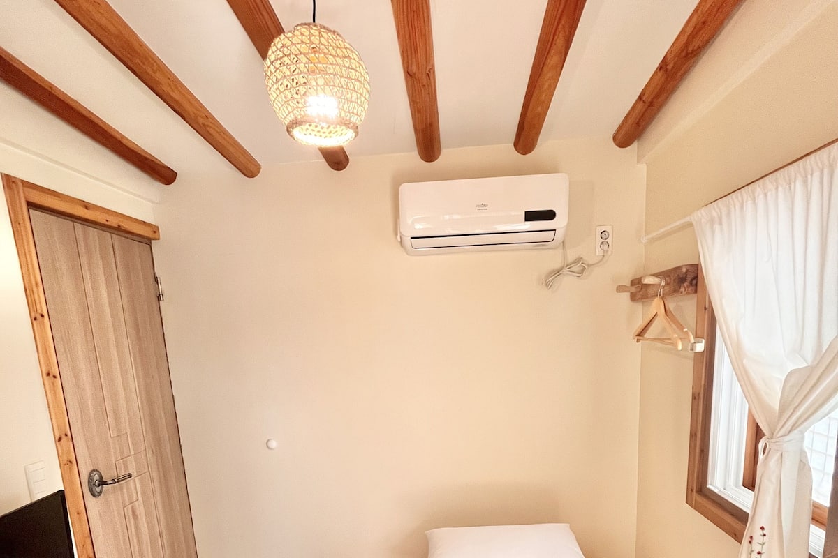 Ein Schlafzimmer mit einem Bett, einer Klimaanlage, einer Hängelampe und einer Holztür.