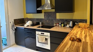A modern kitchen with black cabinets, a stainless steel range hood, a built-in oven, and a wooden countertop. - Très bel Appartement Neuf T4 (Toulon)