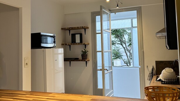 A kitchen with a wooden countertop, white refrigerator, and a window with a view of greenery outside. - Très bel Appartement Neuf T4 (Toulon)