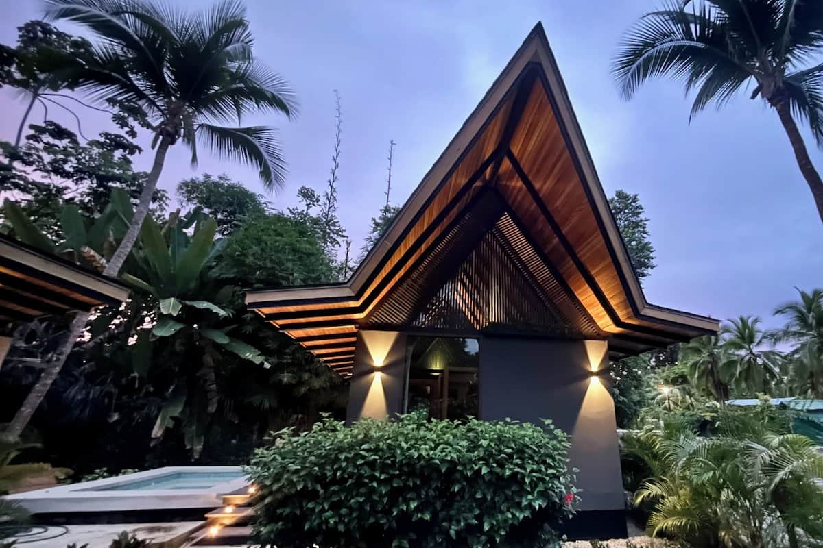 Un bâtiment moderne de forme triangulaire, doté d’une façade en bois et d’un espace piscine situé au premier plan.