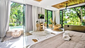 A modern bedroom with a large bed, a flat-screen TV, and a view of lush greenery. - Namu Garden Hotel & Spa - Adults Only (Cahuita)
