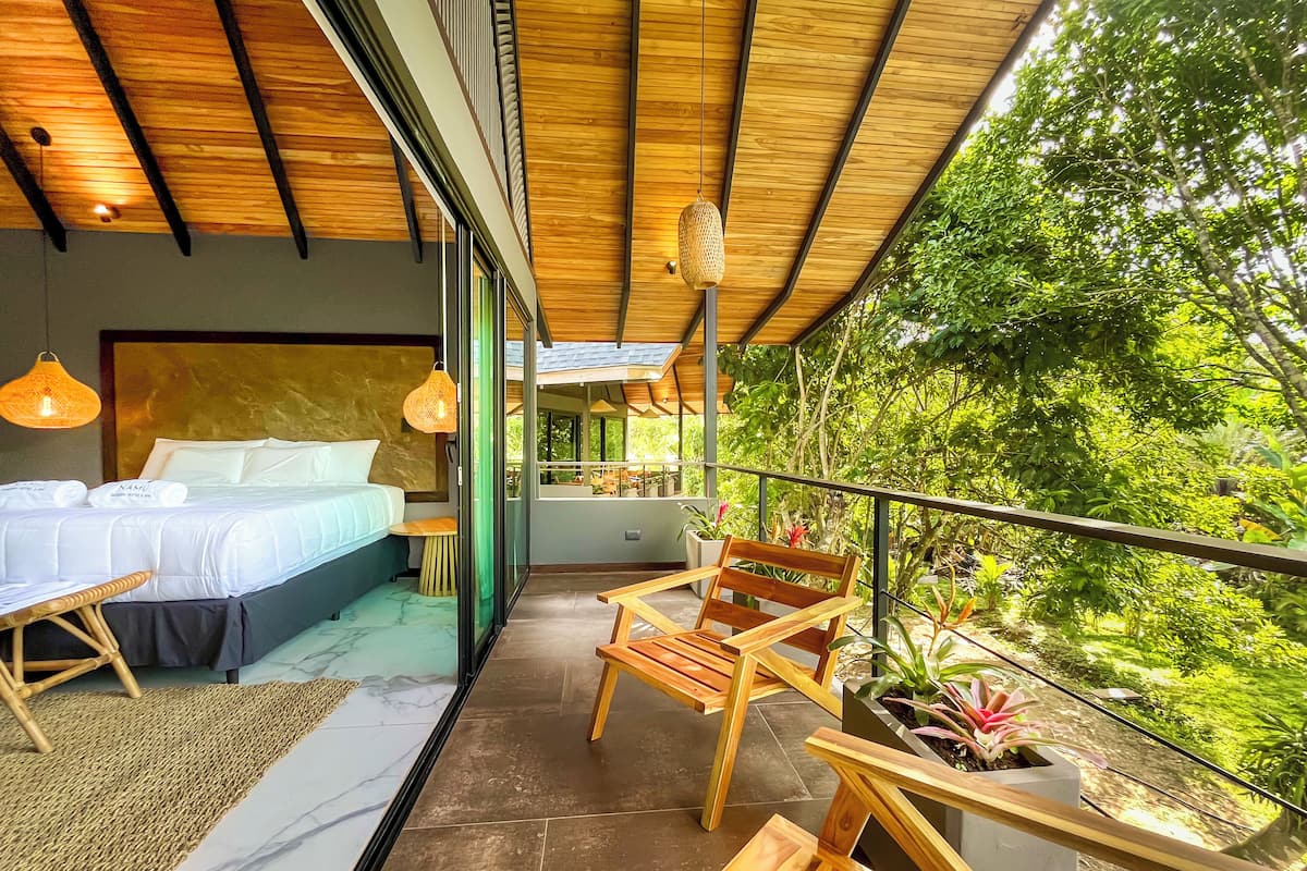 Une chambre moderne avec un grand lit, un plafond en bois et un balcon agrémenté de meubles et de plantes.