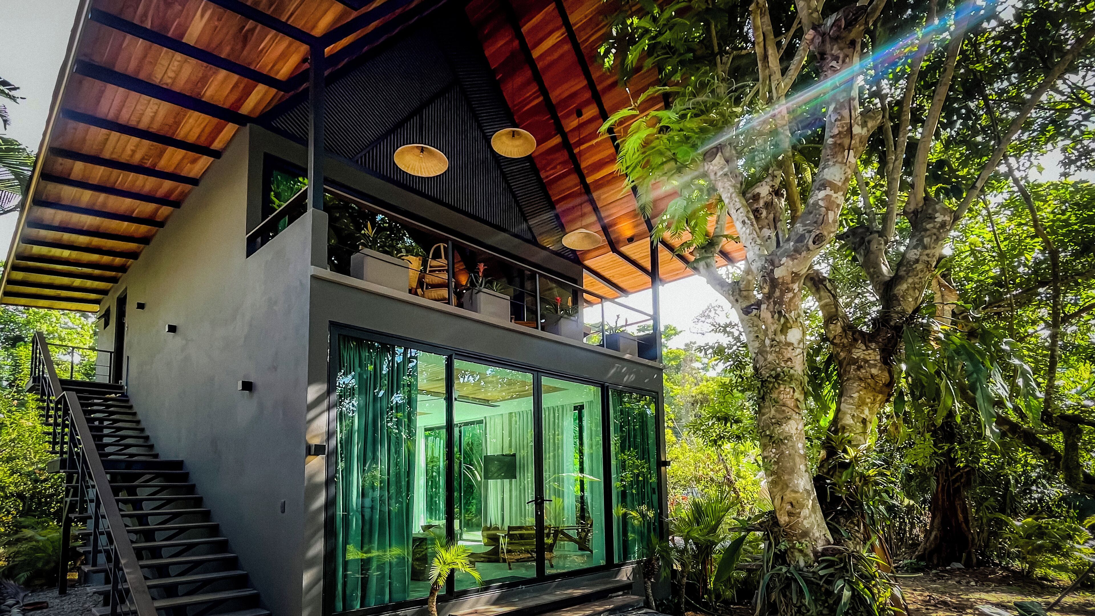 Une maison moderne dotée d’une façade en verre, d’un escalier en bois et offrant une vue sur la forêt environnante.