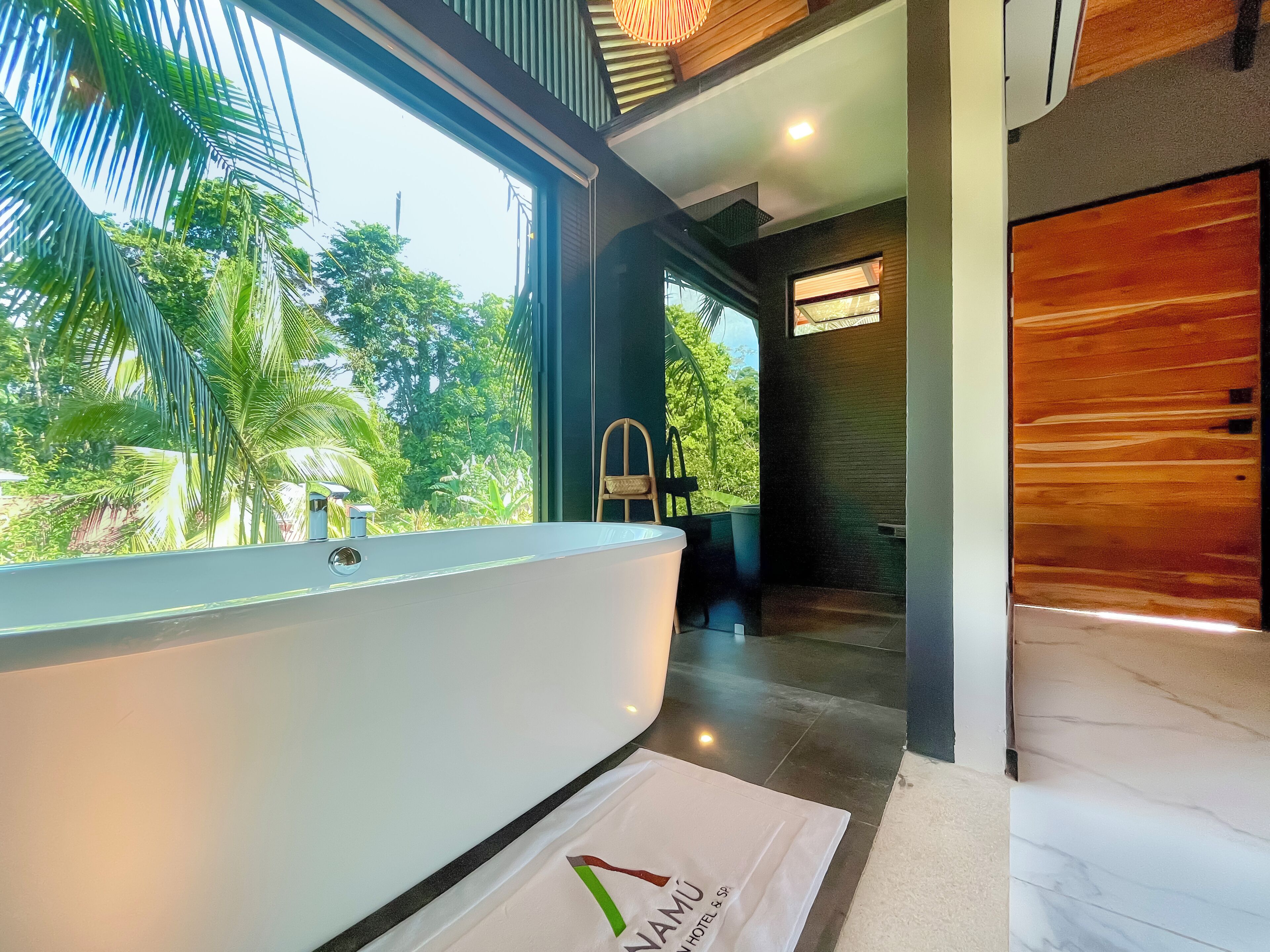 Un baño moderno con una bañera grande, vistas a exuberante vegetación y suelo de madera.